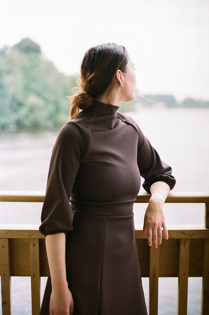 Close up of a model leaning on the guardrail, looking at a river, trees in the background, wearing a polyester dress, neoprene, barefeet.