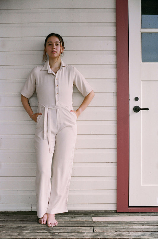 Model standing up, leaning against the wall, looking at the camera, Eggnog coloured jumpsuit, brazilian crepe patou,barefeet