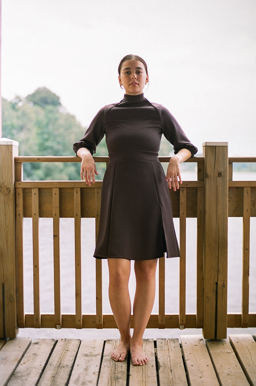 Model leaning on the guardrail, looking at athe camera, a river and trees in the background, wearing a polyester dress, neoprene, barefeet.