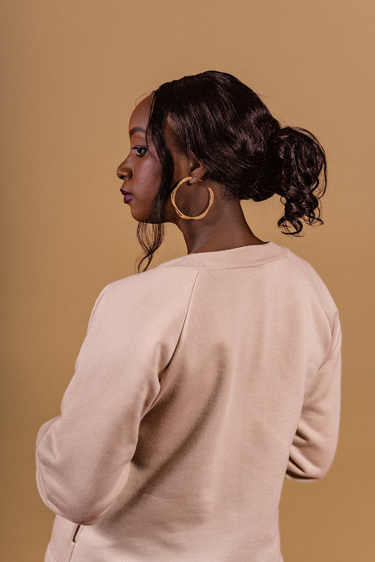 Beije background, model stanting showind her back, face profile, golden earrings,cottom fleece jacket, original 